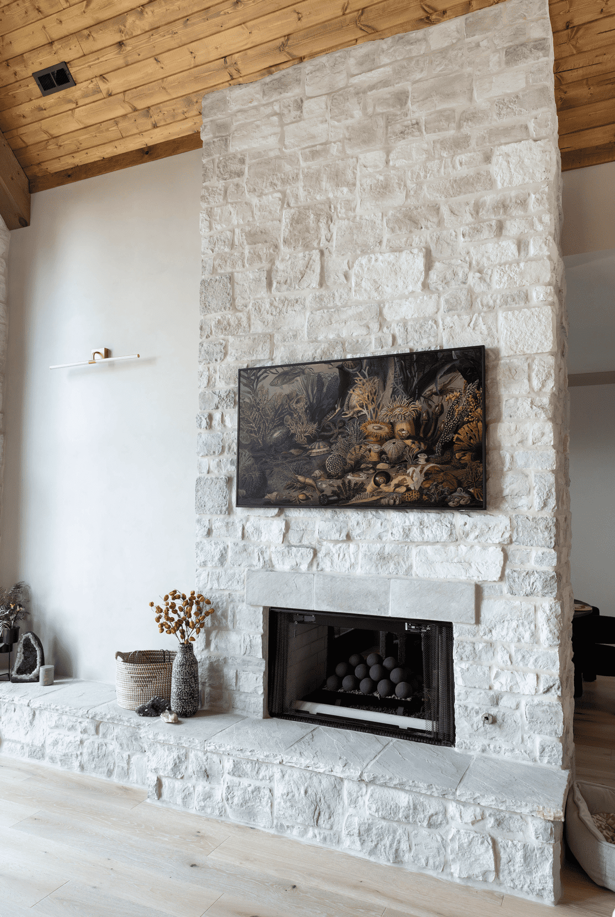 19th-Century-Hermitage-Fireplace-interior Tall stone hearth fireplace with mounted artwork in a modern living room featuring light wood floors and vaulted ceiling