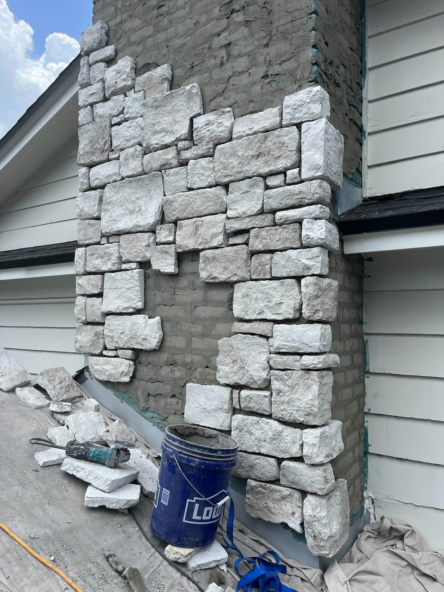 Corner stonework in progress on a garage, mortar and tools staged nearby